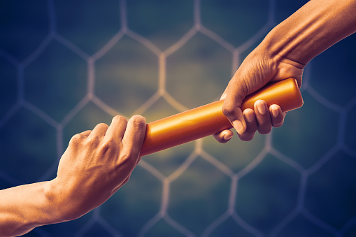 Hands Passing A Relay Baton On On Soccer Goal Net Background With Vintage Color Tone Effect.